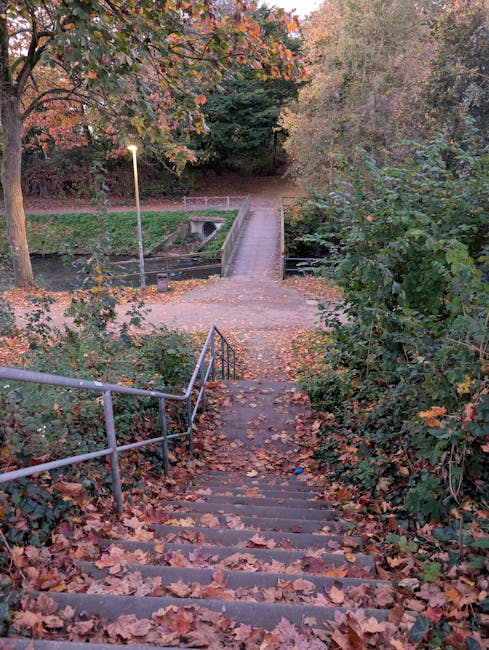A black-and-white photograph depicting an outdoor staircase leading up a residential area, situated between a brick retaining wall on the left and a landscaped garden with bushes and trees on the righ