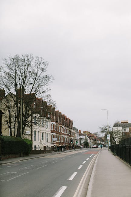 A row of Victorian terrace houses with ornate bay windows, decorative brickwork, and cream-colored exterior facades, situated on a residential street under a partly cloudy sky. In the foreground, a wh