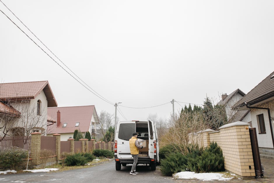 A man wearing a white t-shirt, dark jeans, white sneakers, and a black cap is walking alongside a white delivery van parked on a residential street in Bexleyheath. The van is positioned parallel to th